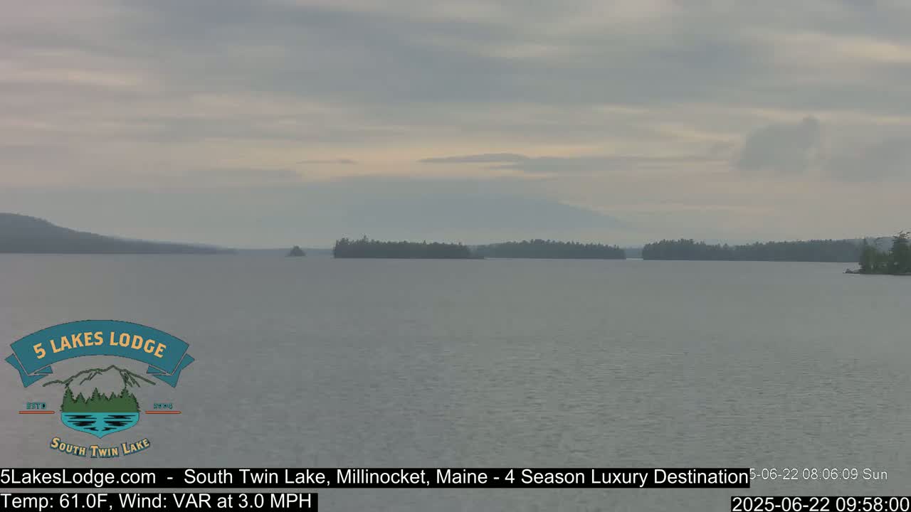A calm lake under an overcast sky, with forested hills visible in the distance.