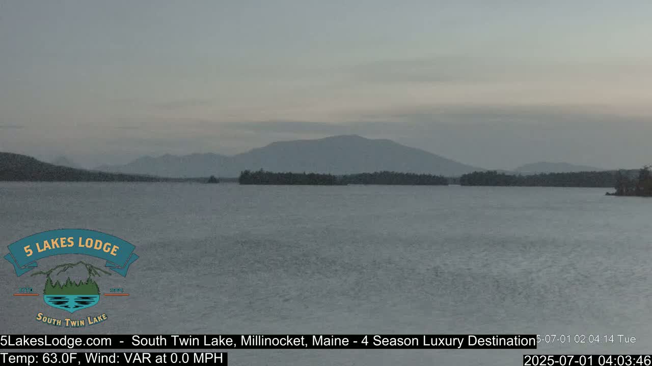 A calm lake with a distant mountain range under an overcast sky.