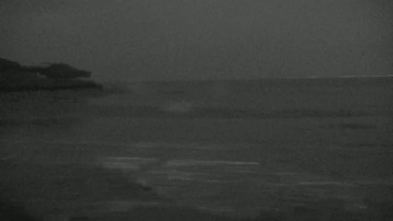 A dark, overcast sky looms over a calm body of water lapping gently against a shoreline.