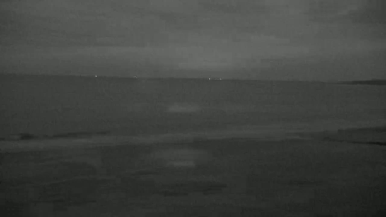 A dark, overcast sky looms over a calm body of water, with a faint shoreline visible in the foreground.