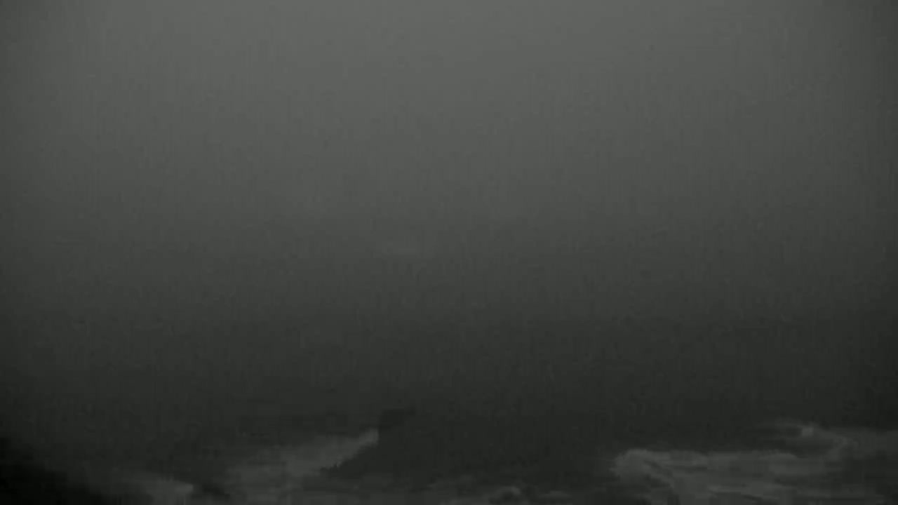 A dark, foggy, and somewhat stormy ocean scene is visible, with waves crashing against what appears to be a rocky shore.