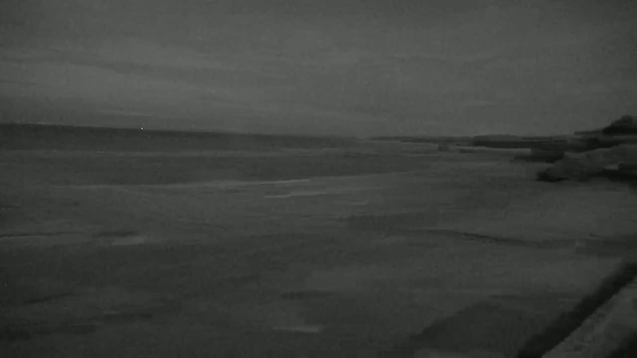 A dark, overcast sky hangs over a calm, gray ocean meeting a dark shoreline.