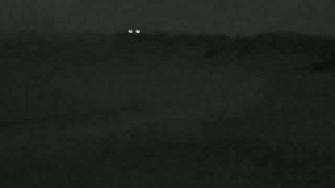 A dark, nighttime landscape is shown with two faint lights in the distance.