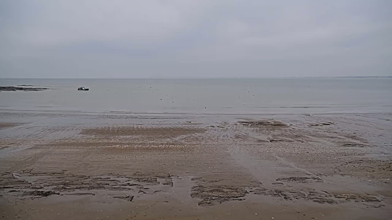 A wide, flat sandy beach stretches to a calm, grey sea under an overcast sky.