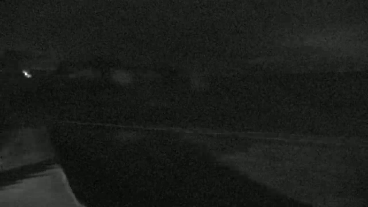 A dark, nighttime scene shows a blurry, indistinct landscape with a faint light source in the distance.