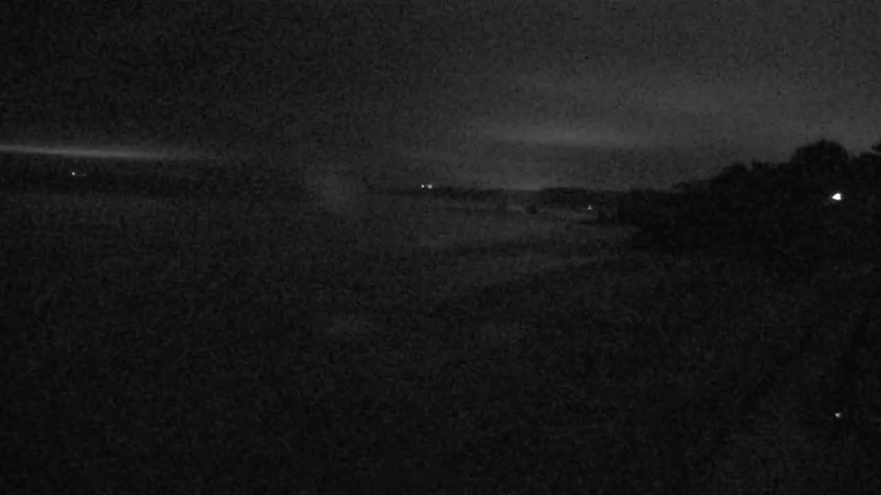 A dark, nighttime landscape shows a few distant lights and a mostly obscured horizon under a cloudy sky.