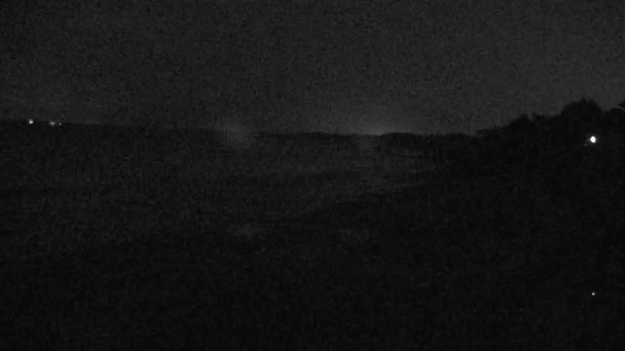 A dark, nighttime landscape is visible, showing a low horizon line with some indistinct shapes possibly representing trees or hills under a mostly clear sky.