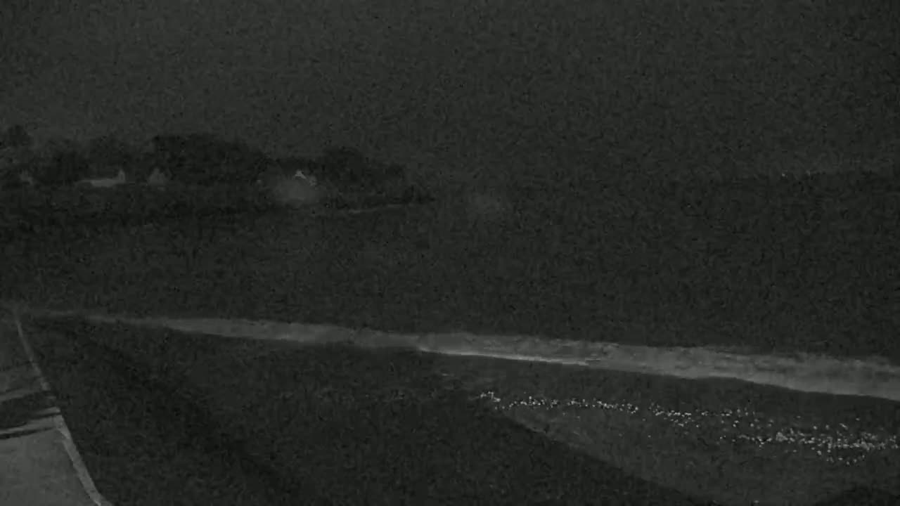 A dark, nighttime scene shows a body of water with a shoreline and a distant landmass under a cloudy sky.