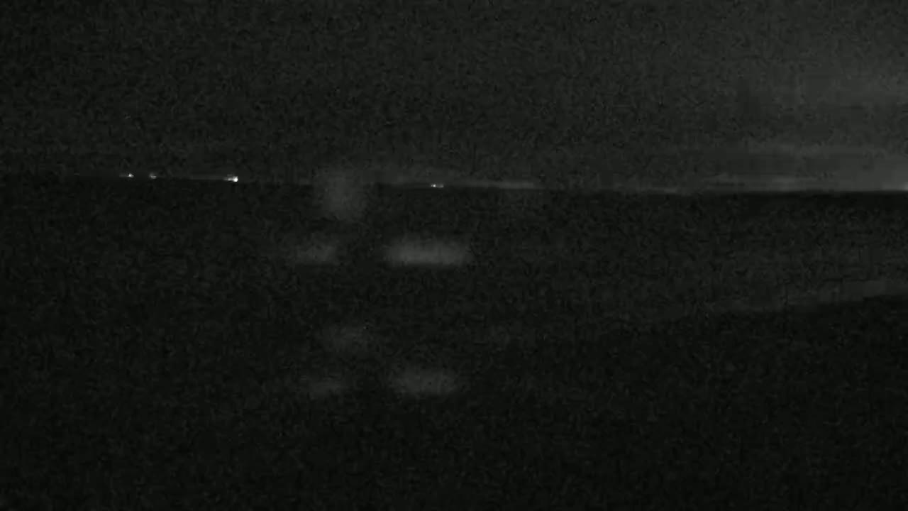 A dark, nighttime scene shows a body of water with a few distant lights visible on the horizon.