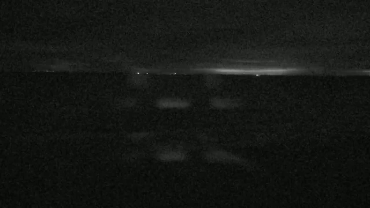 A dark, nighttime view of a body of water with a few faint lights visible on the horizon.