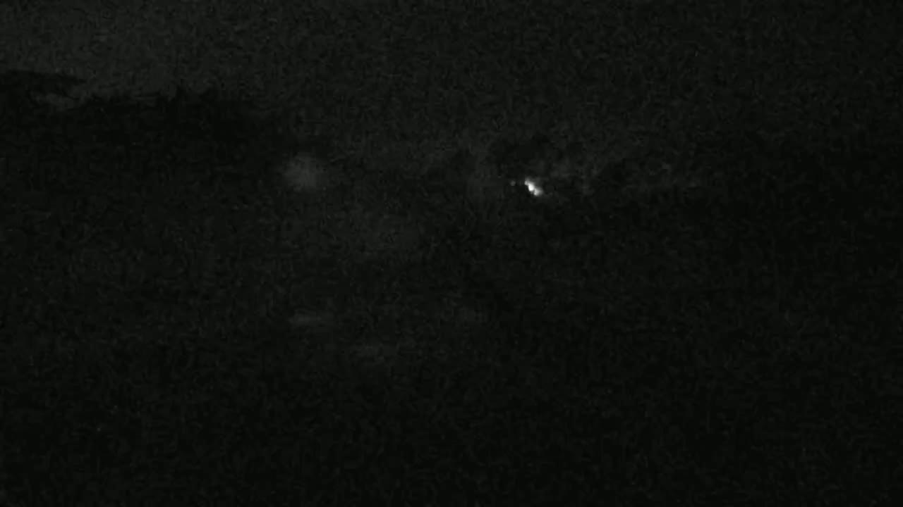 A nighttime, low-light image shows a dark, possibly overcast sky with a faint, distant light source.