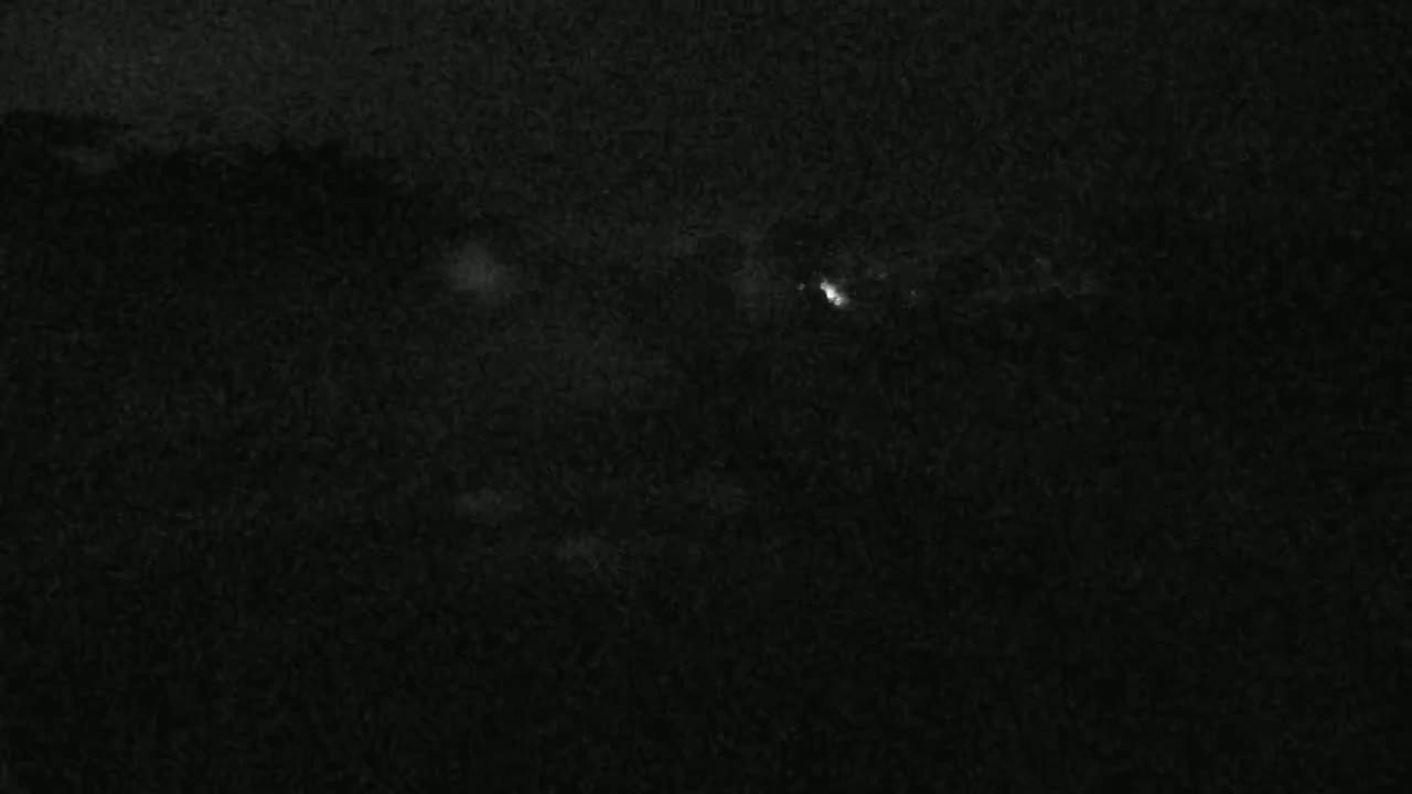 A dark, nighttime scene shows a few faint lights in the distance.