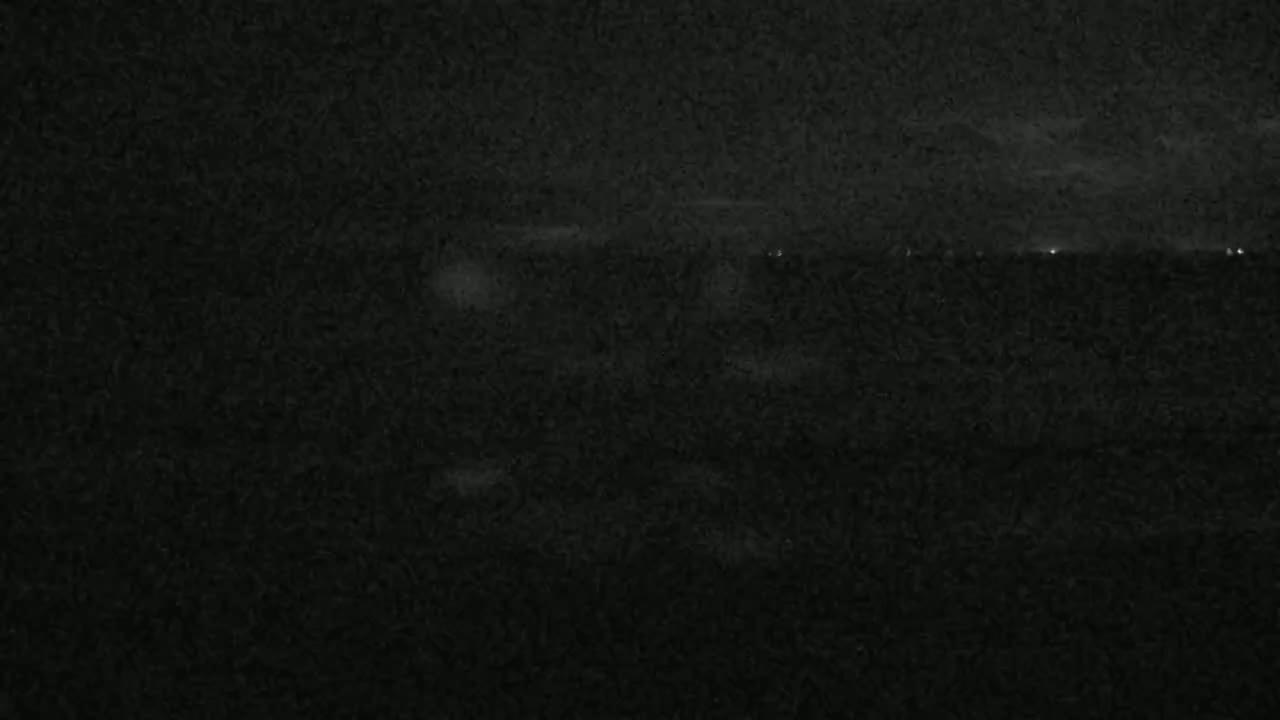 A dark, nighttime scene shows a blurry, indistinct landscape with a few faint lights visible in the distance.