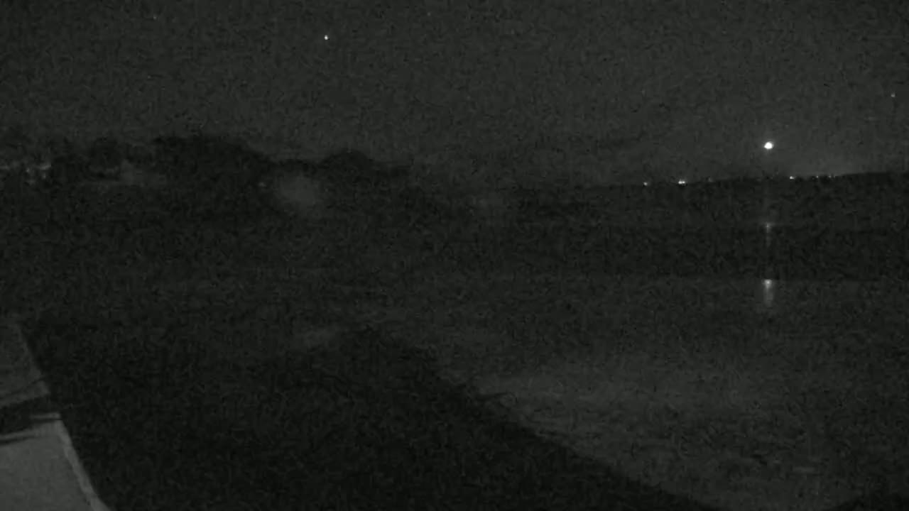 A nighttime, low-light view shows a dark landscape with a few distant lights under a mostly clear, starry sky.