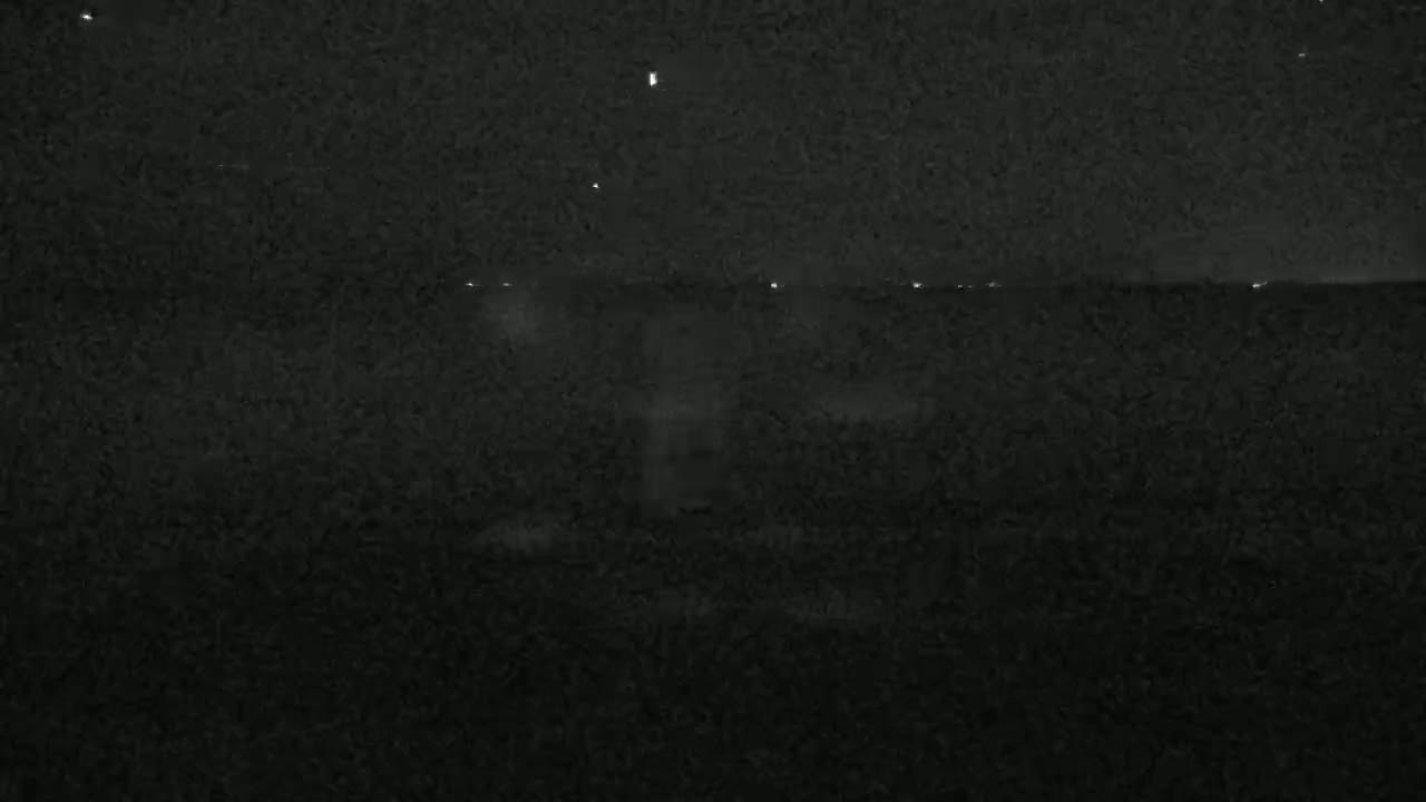 A dark, nighttime scene shows a dimly lit horizon line with a few distant lights.