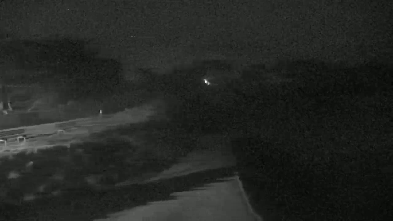 A nighttime, low-light image shows a dark landscape with a road and some indistinct objects, possibly trees or buildings.