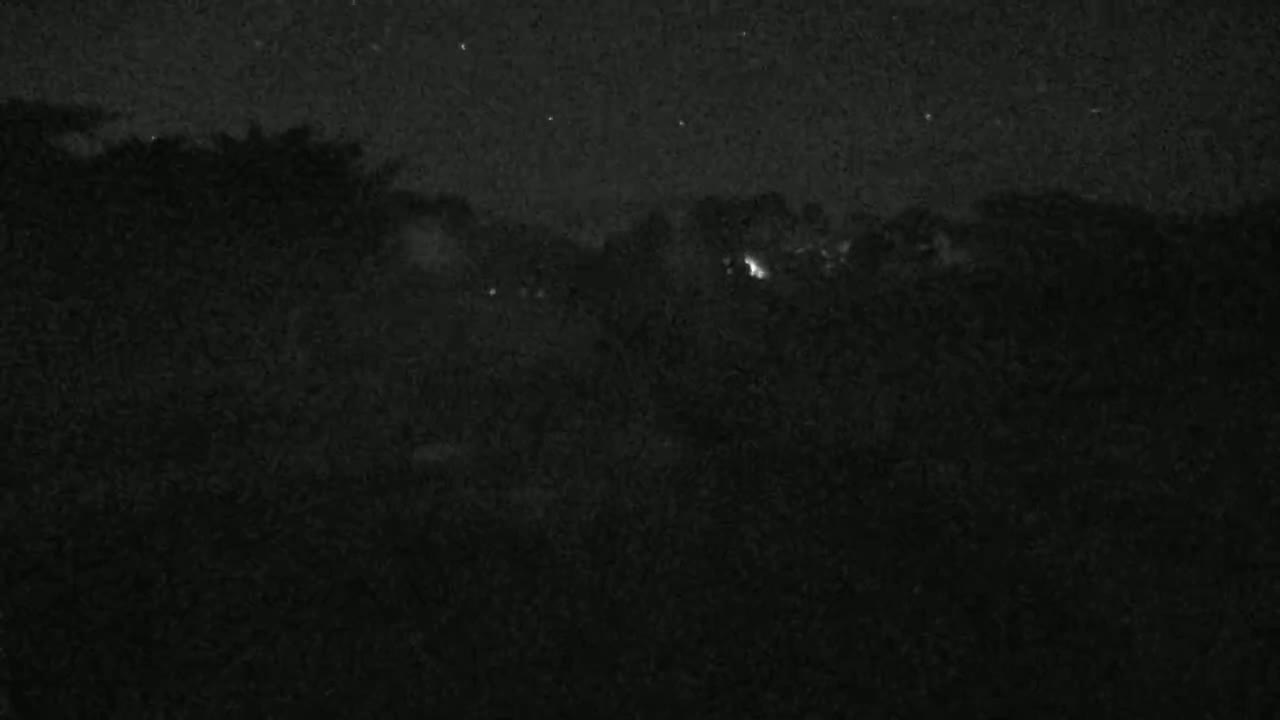 A nighttime, low-light view shows a dark, silhouetted landscape under a slightly starry sky.