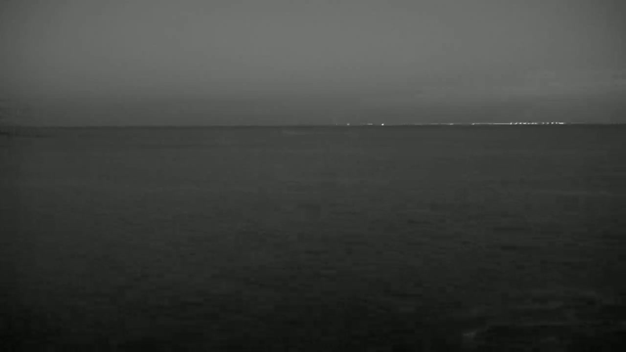 A dark, calm body of water is shown at night with faint lights visible on the horizon.