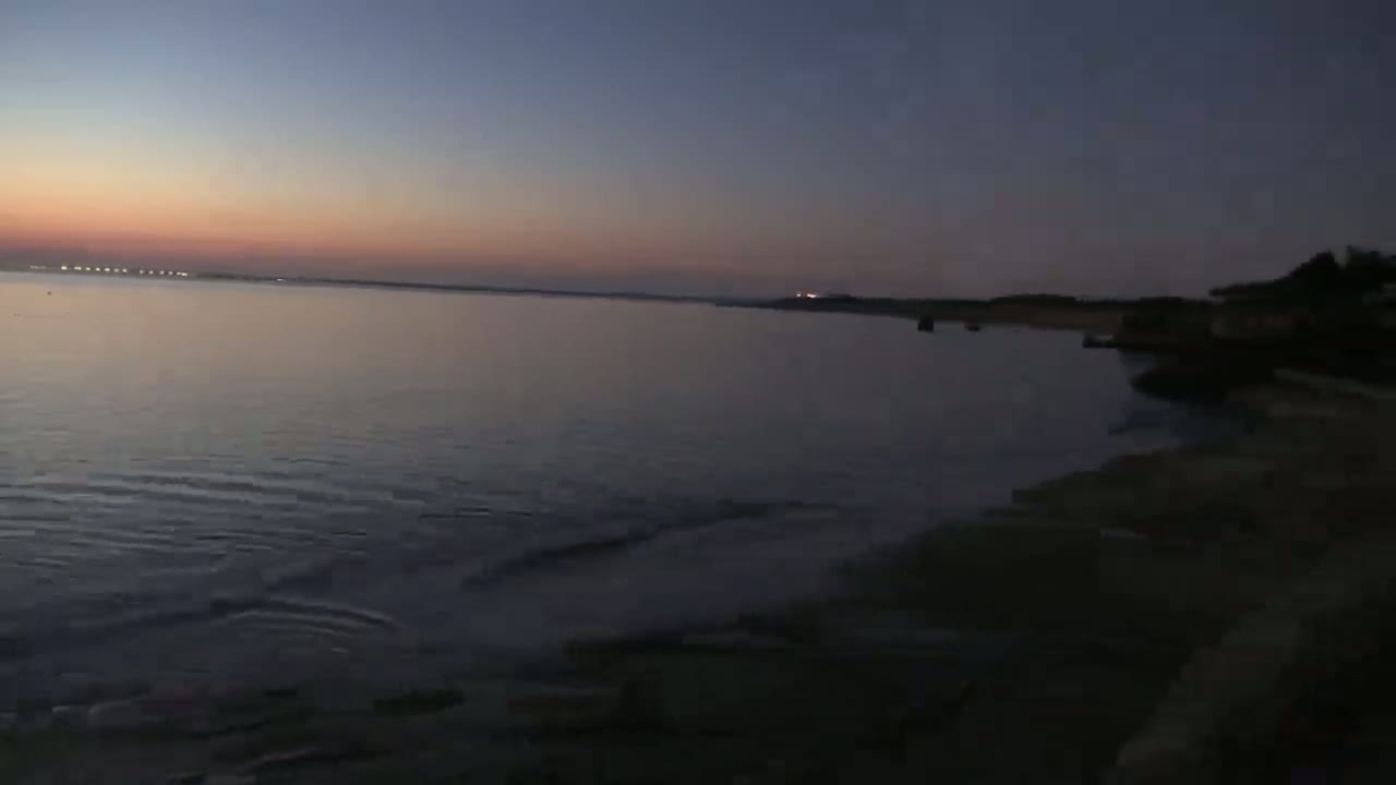 Gentle waves lap a dark shoreline at dusk, under a twilight sky.