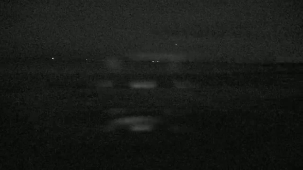 A nighttime, blurry view of a dark landscape with a few faint lights in the distance.
