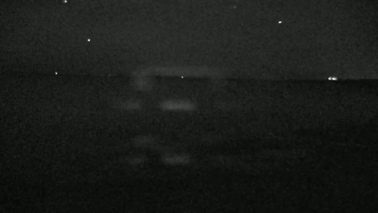 A dark, nighttime scene shows a body of water under a mostly clear sky with a few visible stars.