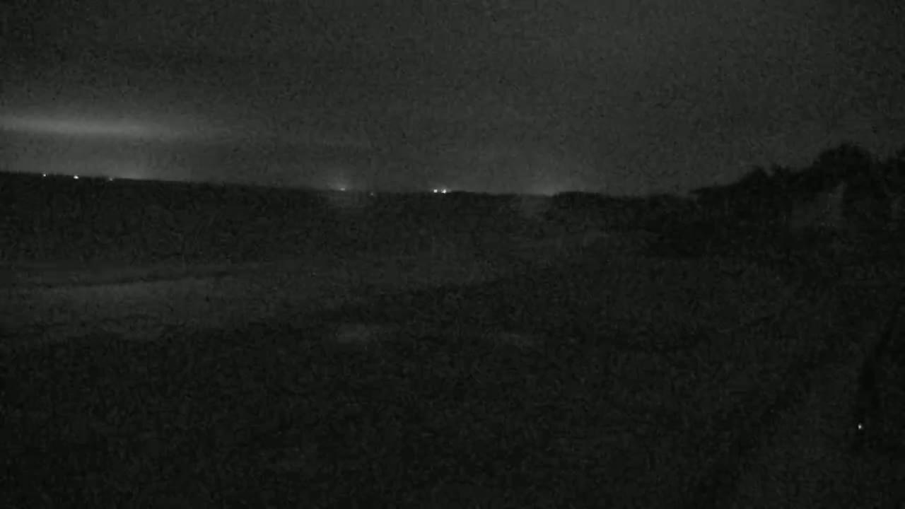 A dark, nighttime landscape is visible, showing a flat expanse of land with a few distant lights under a cloudy sky.