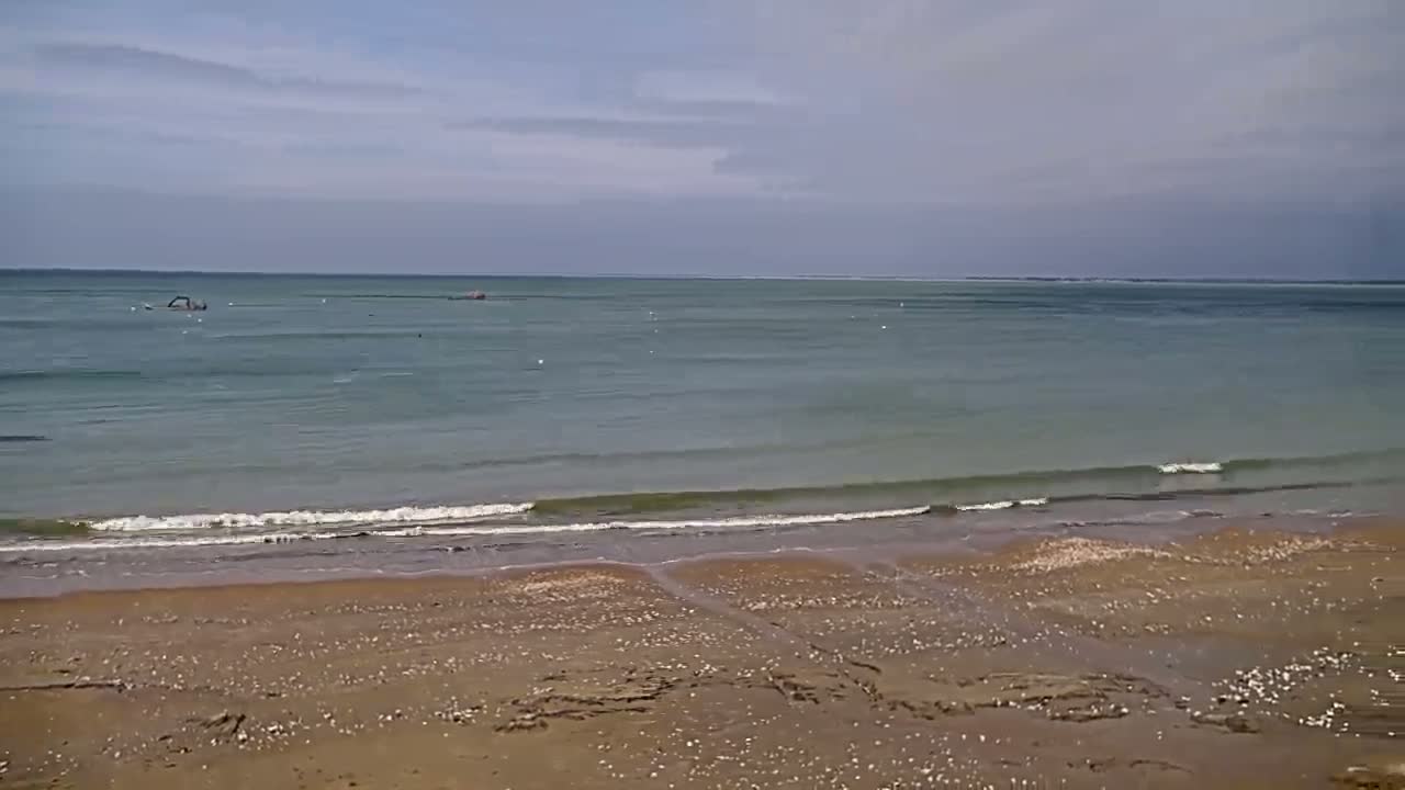 A sandy beach with small waves lapping the shore under a partly cloudy sky.