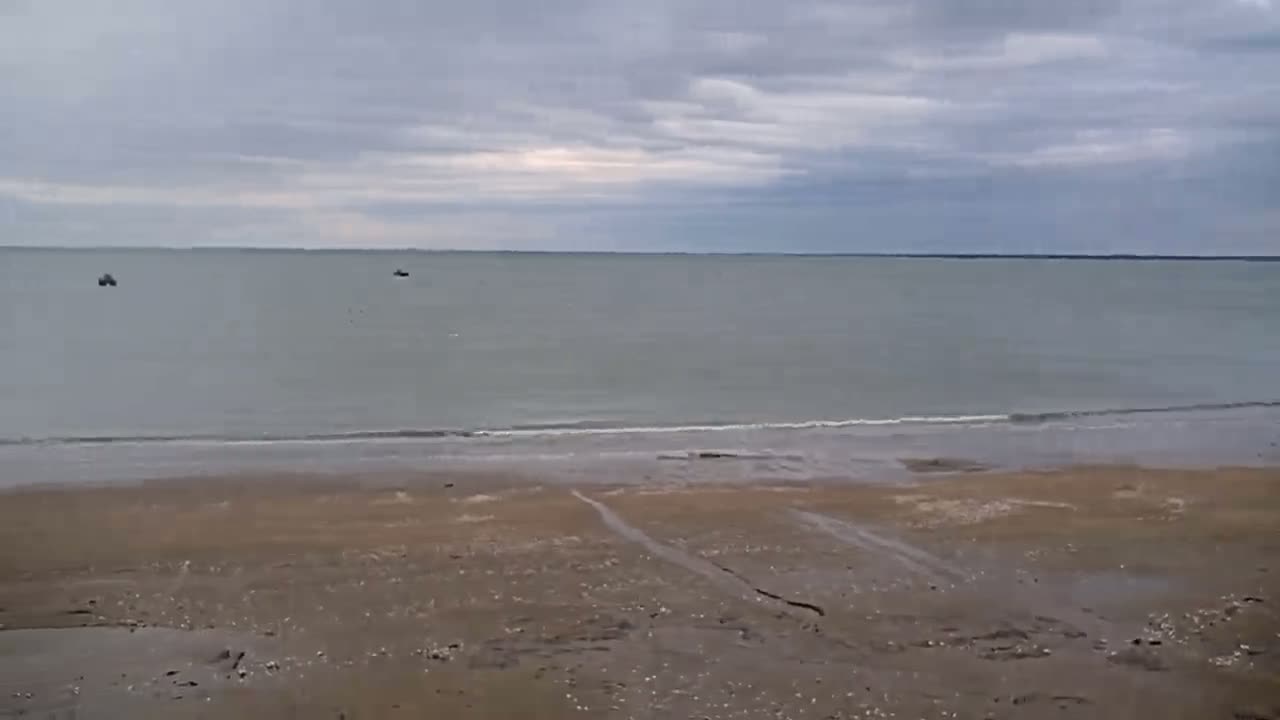 A sandy beach stretches to a calm, gray sea under an overcast sky.