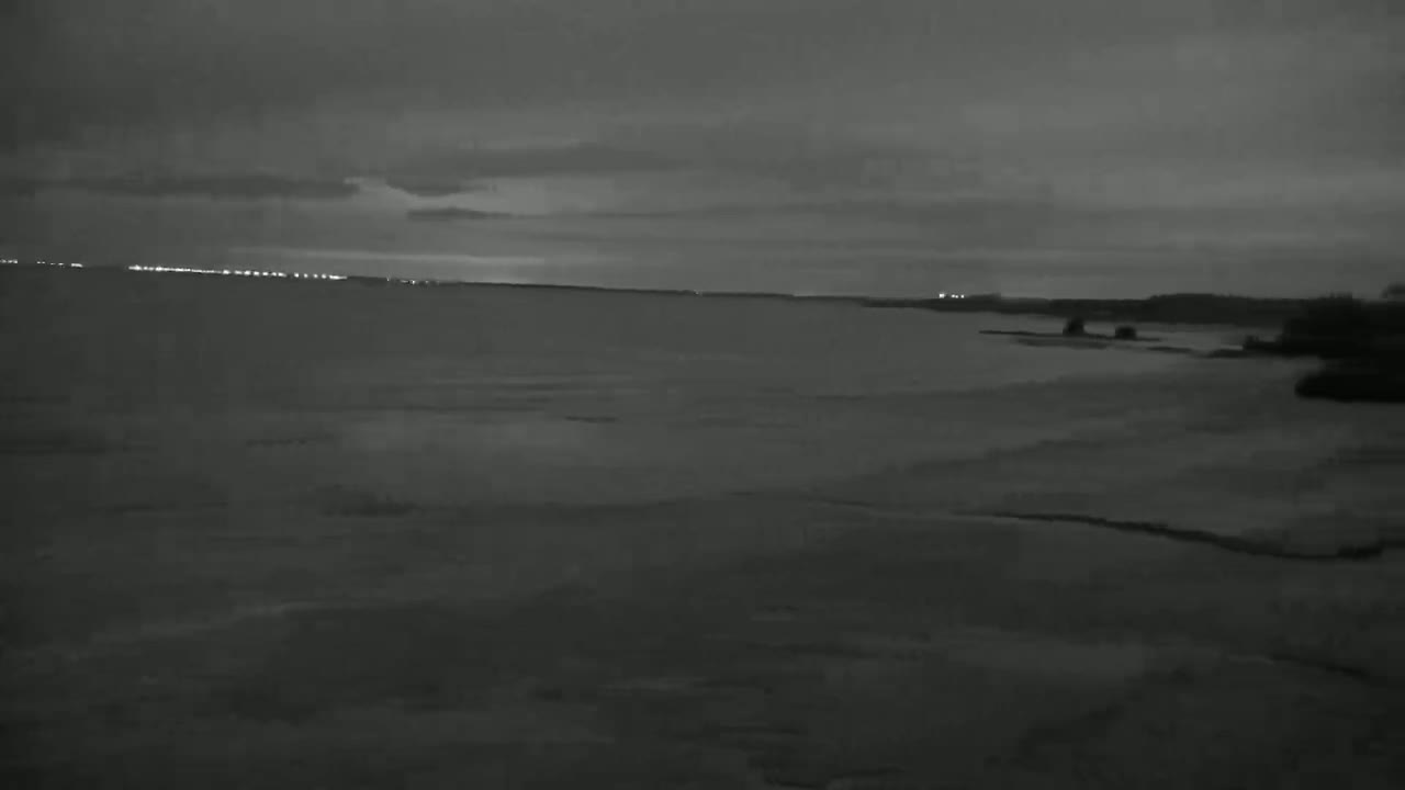 A dark, overcast sky hangs over a calm body of water, with a distant shoreline barely visible under the dim light.