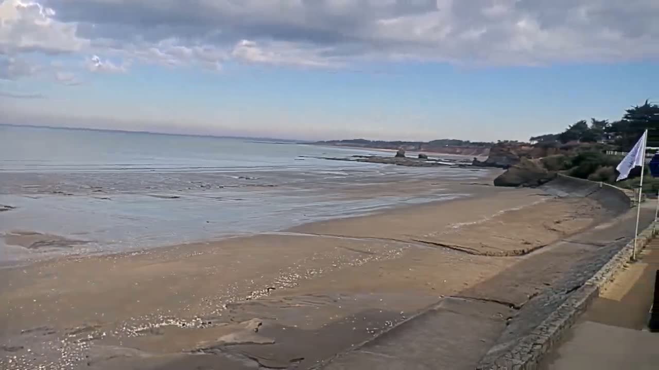 A wide sandy beach stretches out to a calm sea under a partly cloudy sky.