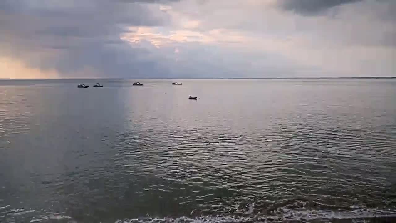 Several small boats are visible on a calm, grey sea under a cloudy sky.