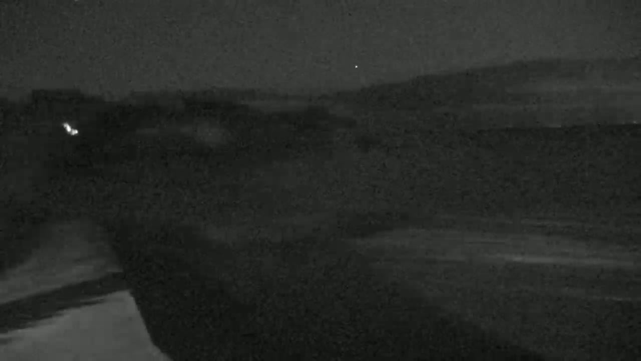 A nighttime, low-light image shows a dark, flat landscape under a clear sky with a few visible stars.