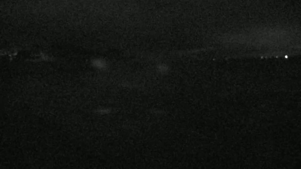 A dark, nighttime scene shows a mostly featureless expanse with a faint, distant line of lights on the horizon.