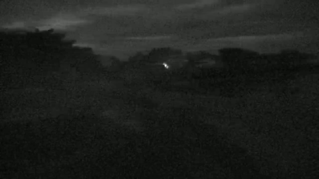 A dimly lit, dark landscape is visible under a cloudy night sky, with a single point of light in the mid-ground.