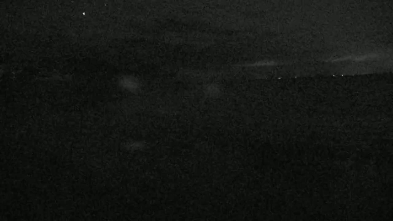A nighttime, low-light image shows a dark, textured landscape under a mostly clear sky.