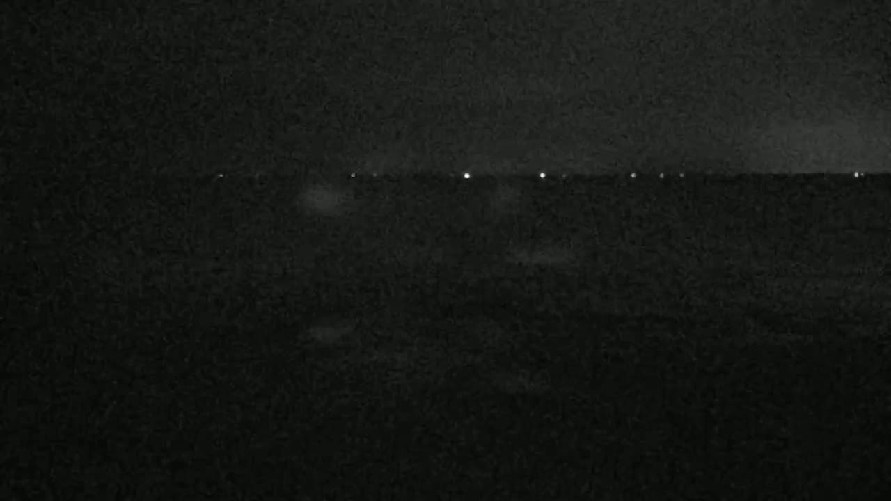 A dark, nighttime landscape is shown with a line of faint lights on the horizon.
