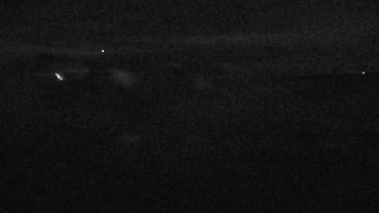 A dark, night-time scene shows a few faint lights in the distance under a mostly clear sky.