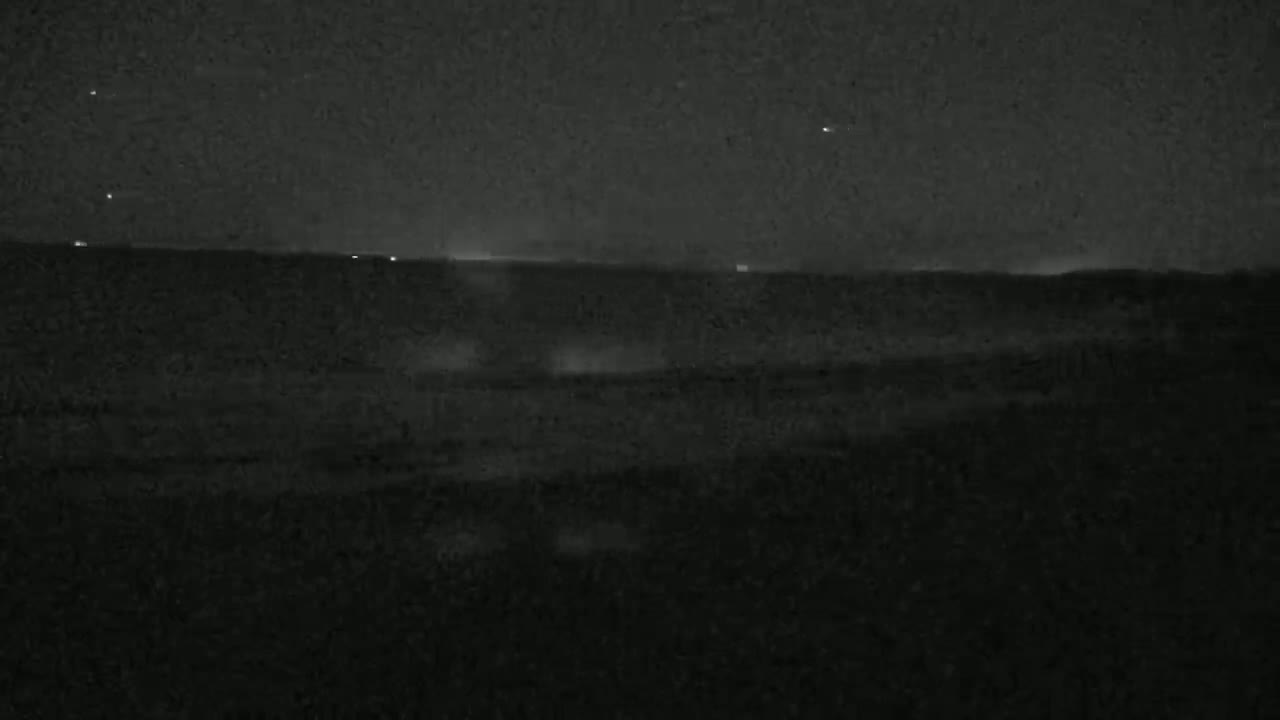 A dark, nighttime landscape is visible, showing a flat horizon with a few distant lights under a clear, starlit sky.