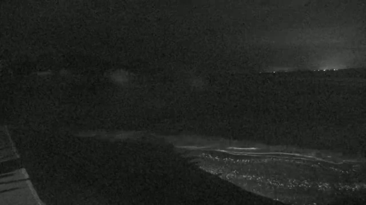 A nighttime, low-light view of a dark, possibly coastal, area with faint lights visible in the distance.
