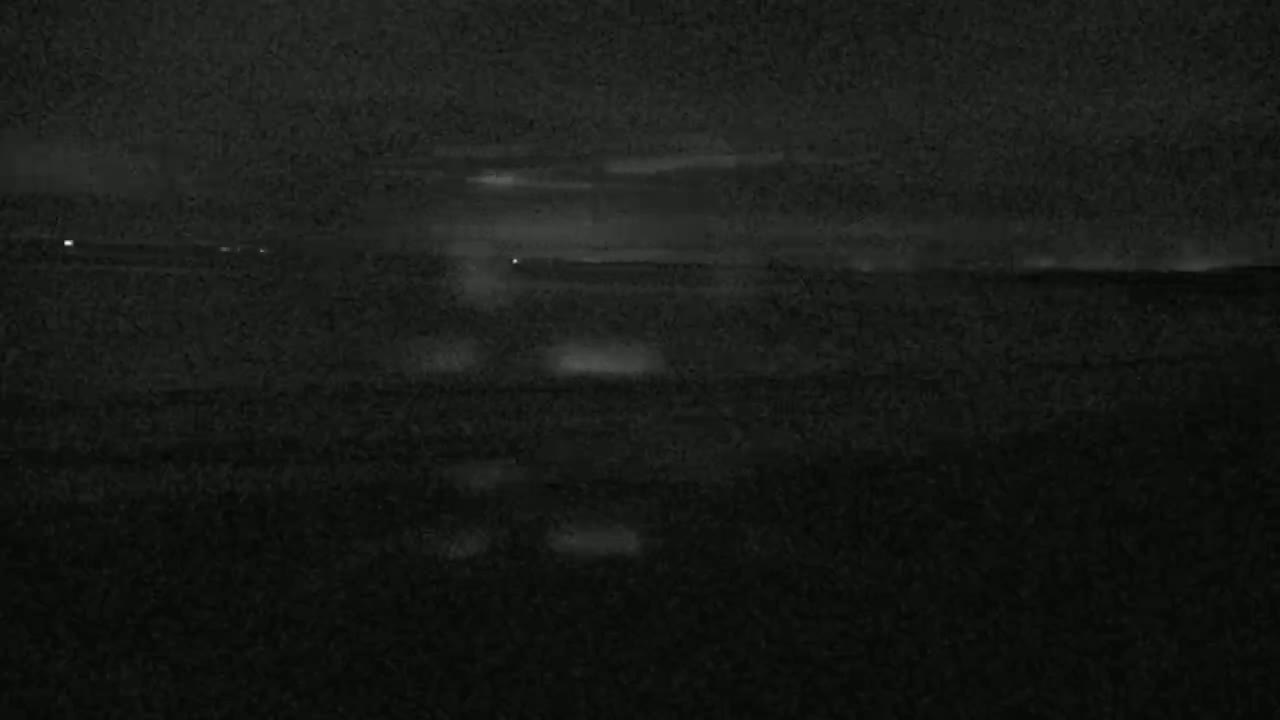A dark, nighttime scene shows a flat, dark expanse of land or water under a cloudy sky.