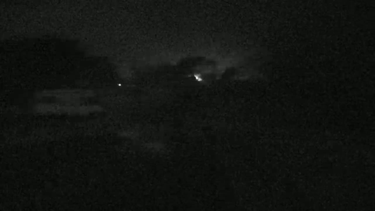 A nighttime outdoor scene shows a dark, cloudy sky with a faint lightning strike in the distance.