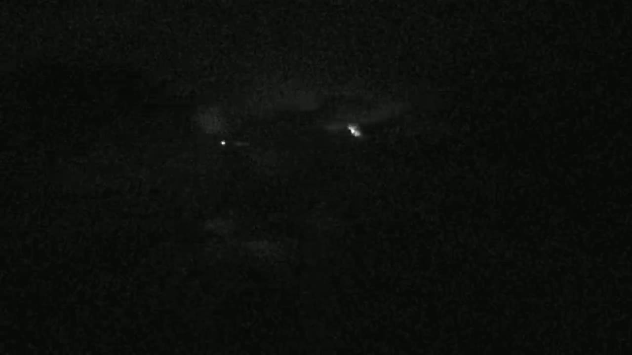 A nighttime, dark, grainy image shows a few faint lights in the distance.