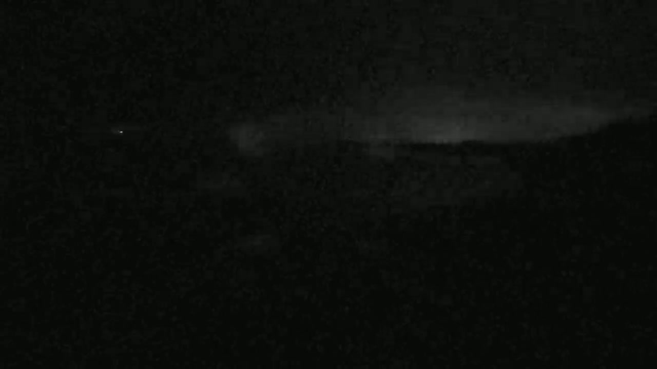 A dark, nighttime landscape is visible, with a faintly illuminated horizon suggesting a cloudy sky.
