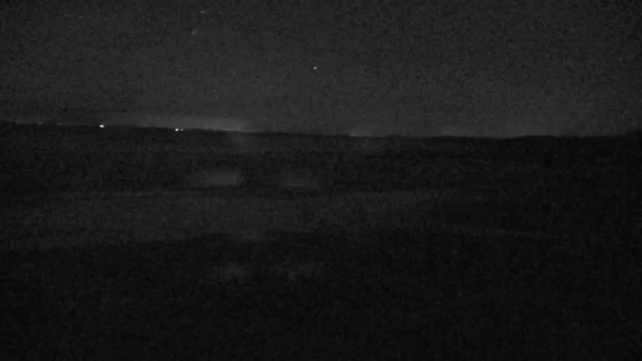 A dark, nighttime landscape is visible, showing a flat horizon line with a few distant lights under a clear, starry sky.