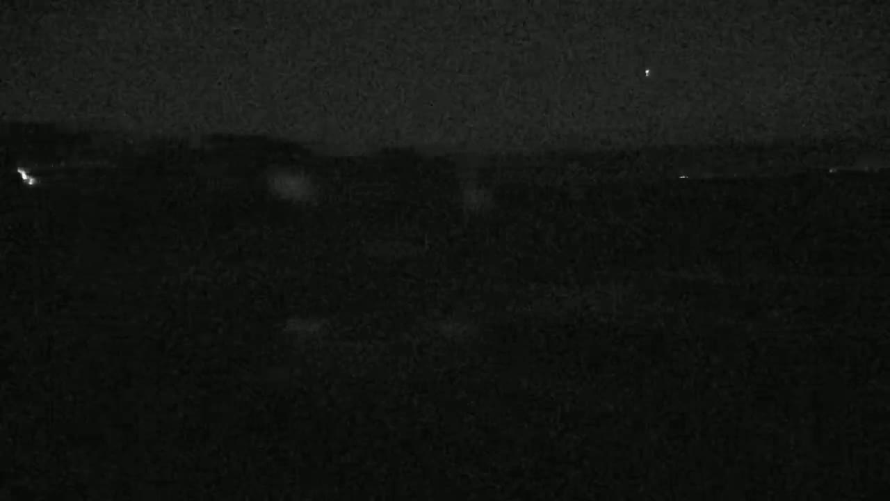 A nighttime, low-light view shows a dark landscape with a few distant lights and a possibly stormy sky.