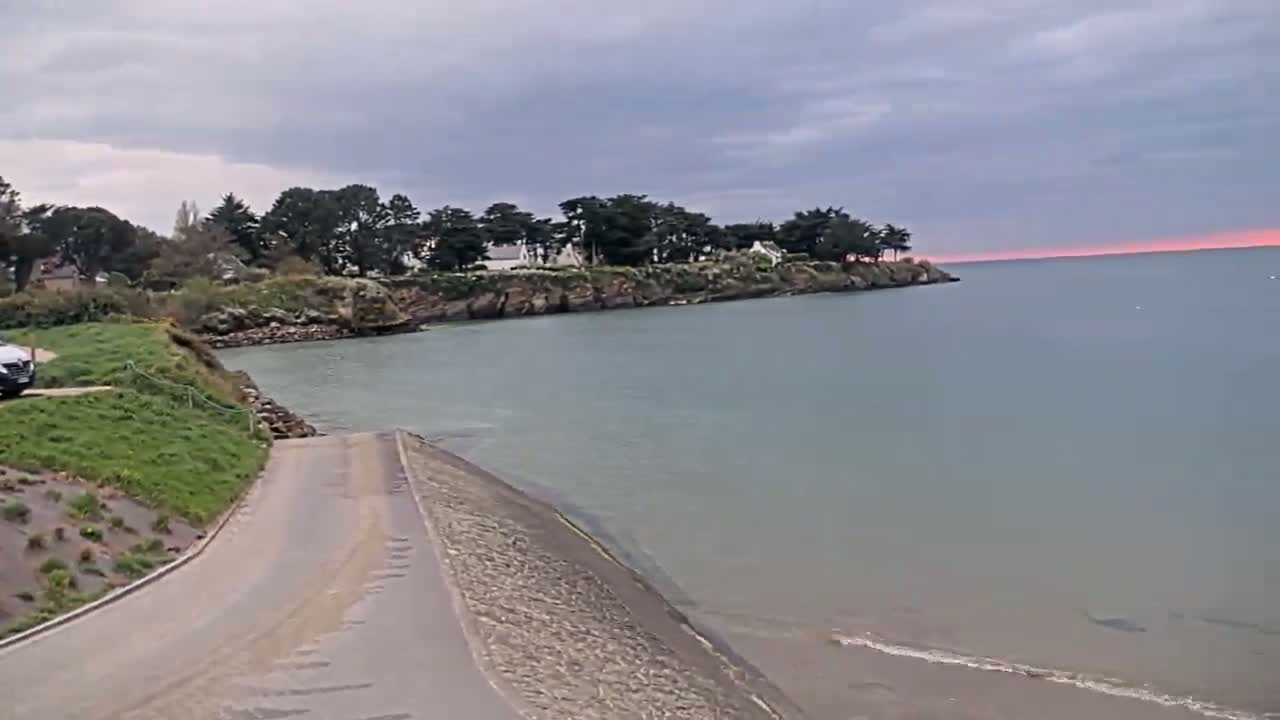A paved boat ramp leads down to a calm body of water under a cloudy sky with a hint of pink on the horizon.