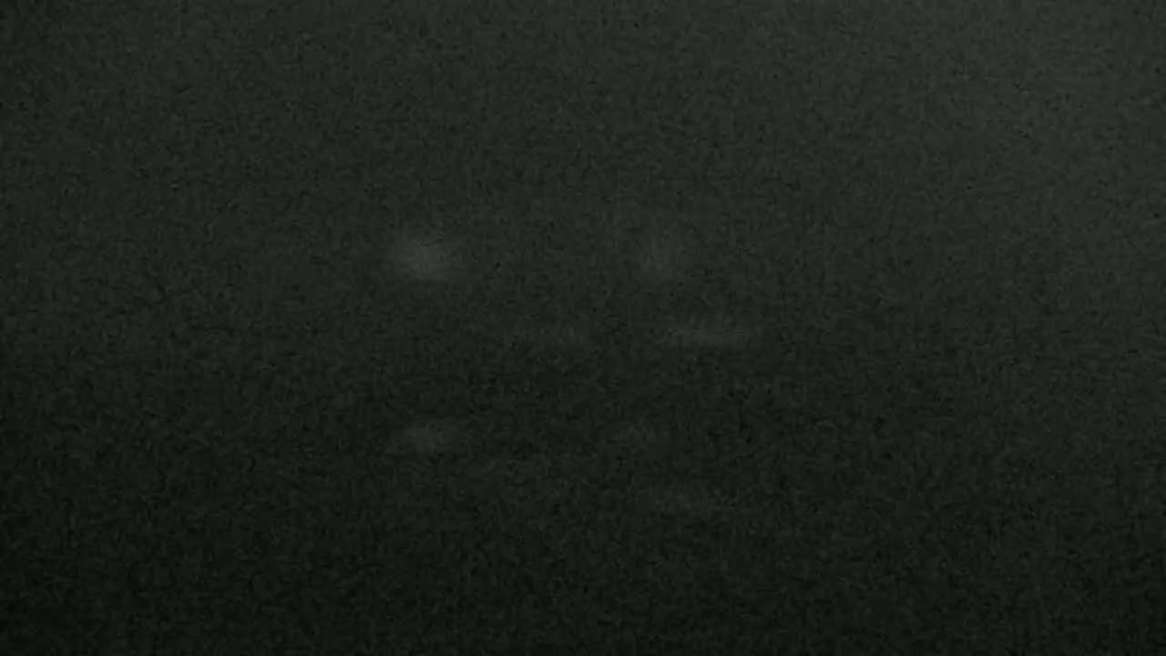 A dark gray textured surface with faint, lighter gray marks scattered across it.