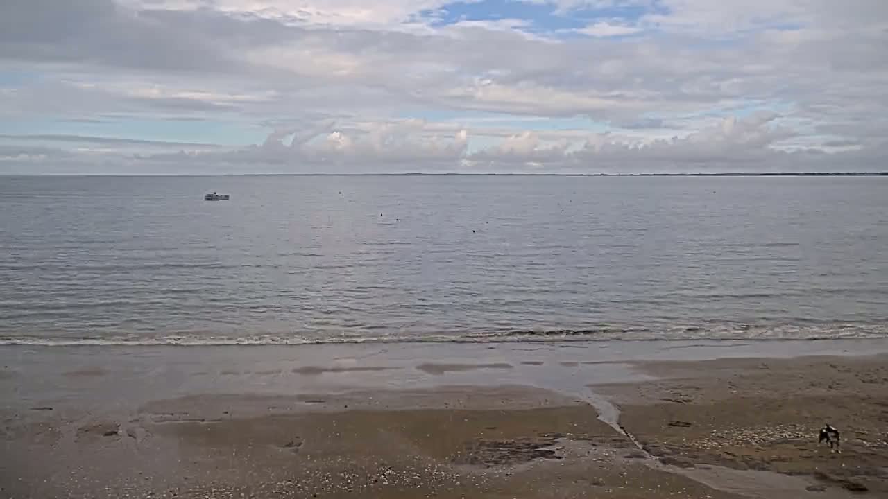 A sandy beach with a calm sea under a partly cloudy sky, and a single small boat visible on the water.