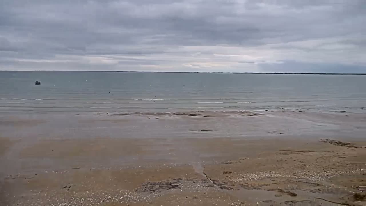 A sandy beach stretches to a calm, gray sea under a cloudy sky.