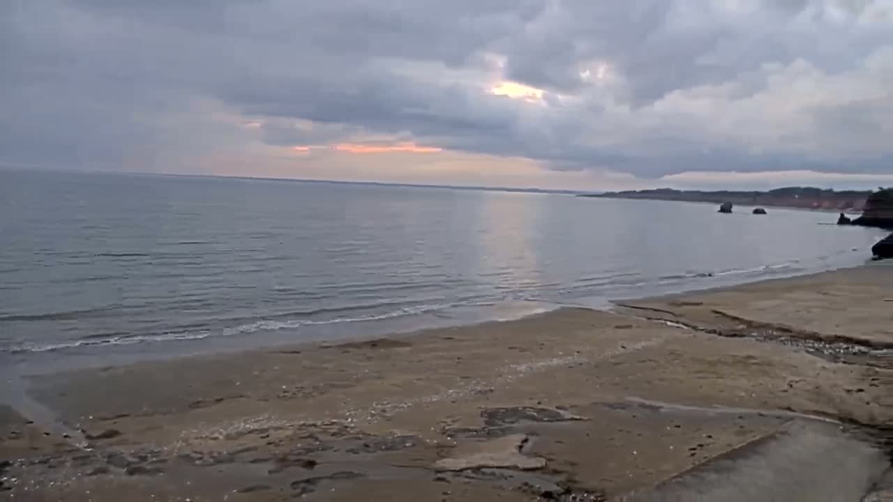 A sandy beach stretches towards a calm sea under a cloudy sky with hints of sunset.